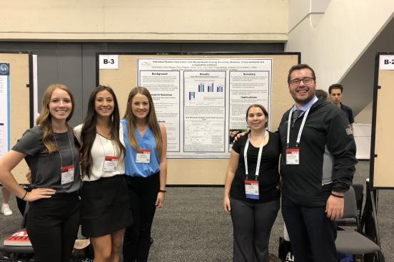 Five students standing in front of a poster at a conference
