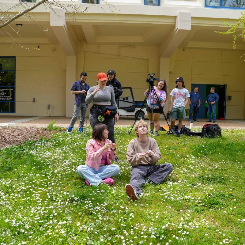 Actors sitting on lawn in front of camera crew