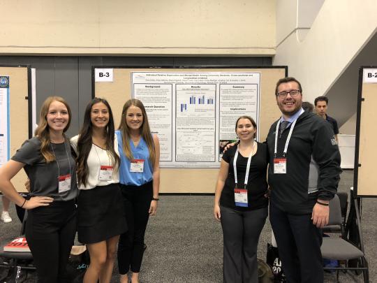 Five students standing in front of a poster at a conference